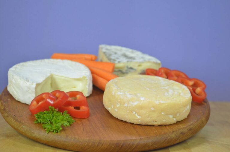 Drei Käsesorten auf einem Holzbrett: Weichkäse, Blauschimmelkäse und Schnittkäse, garniert mit Paprika, Möhren und Petersilie